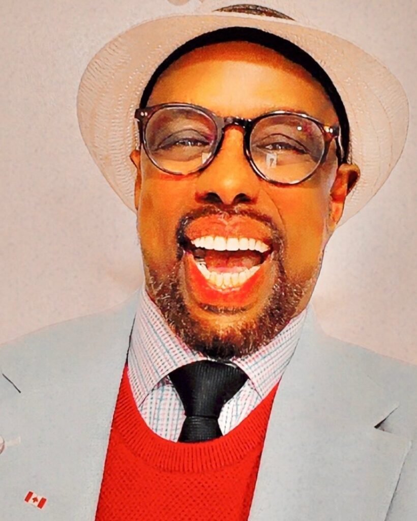 Chairman Ibrahim Shurie laughing, wearing a pale hat, grey jacket and red sweater