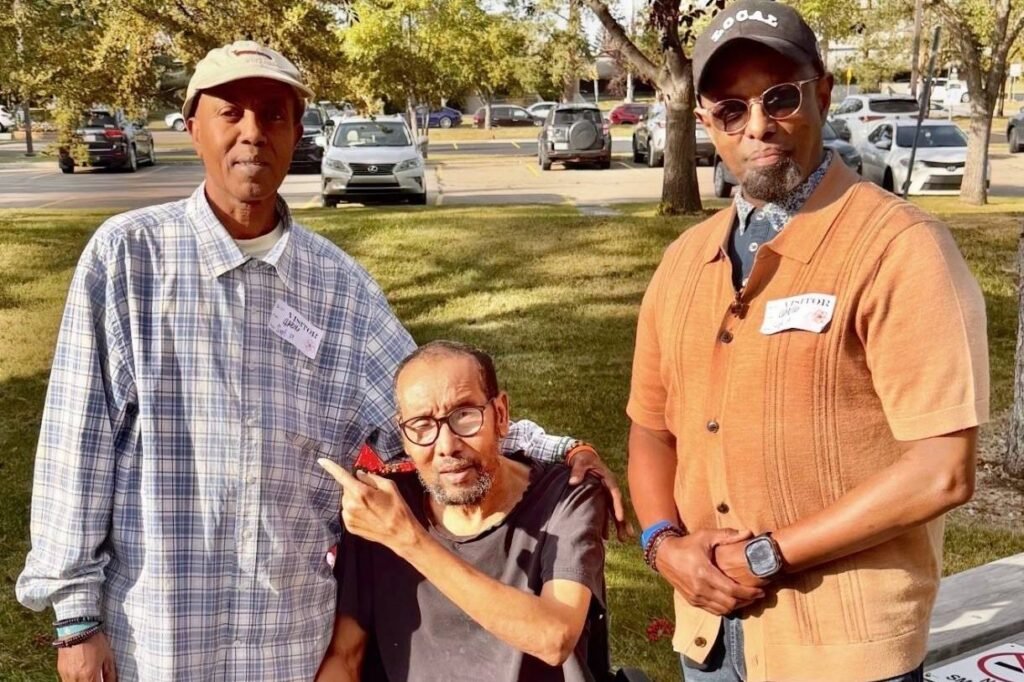 Chairman Ibrahim Shurie and another visitor standing with a community member in a wheelchair outside a care facility