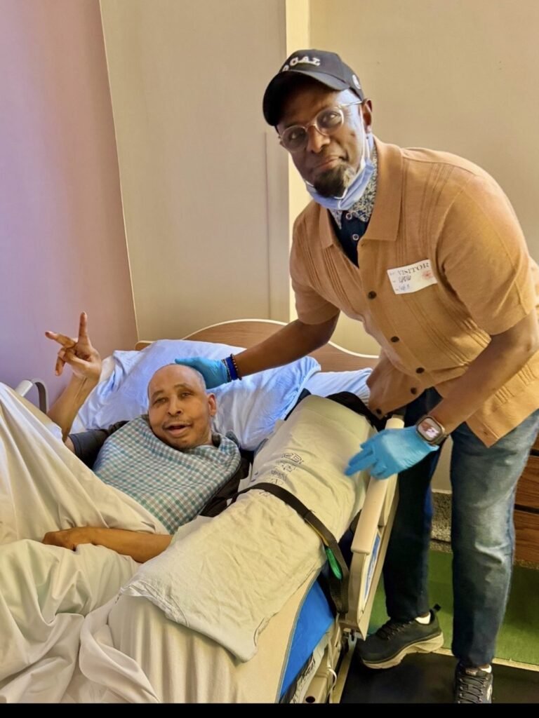 Chairman Ibrahim Shurie greeting a community member resting in a hospital bed