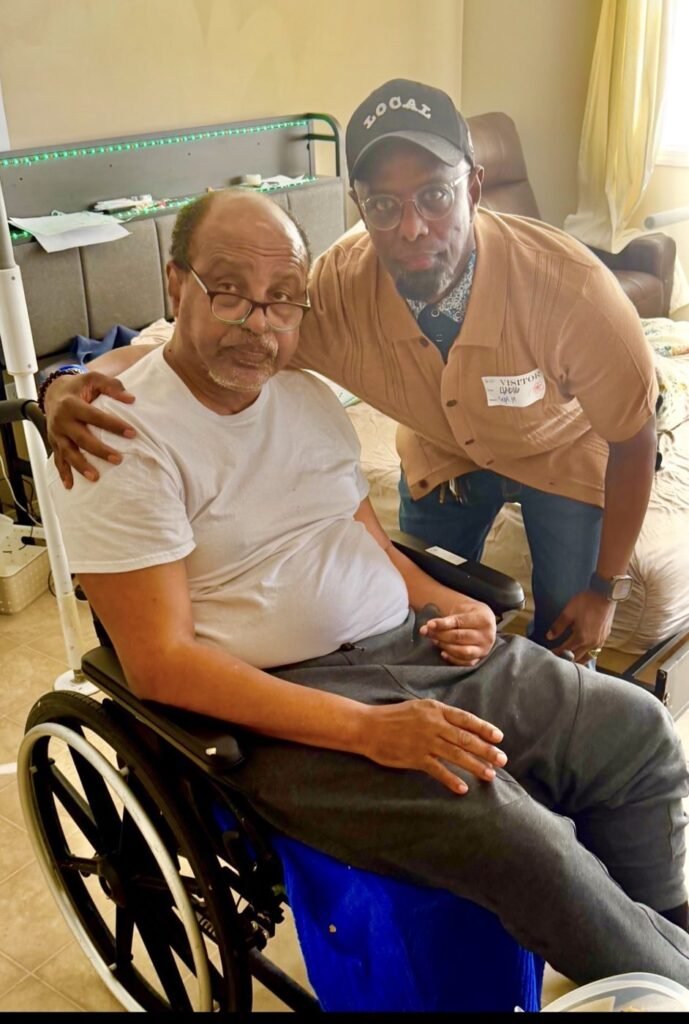 Chairman Ibrahim Shurie with a community member seated in a wheelchair at home
