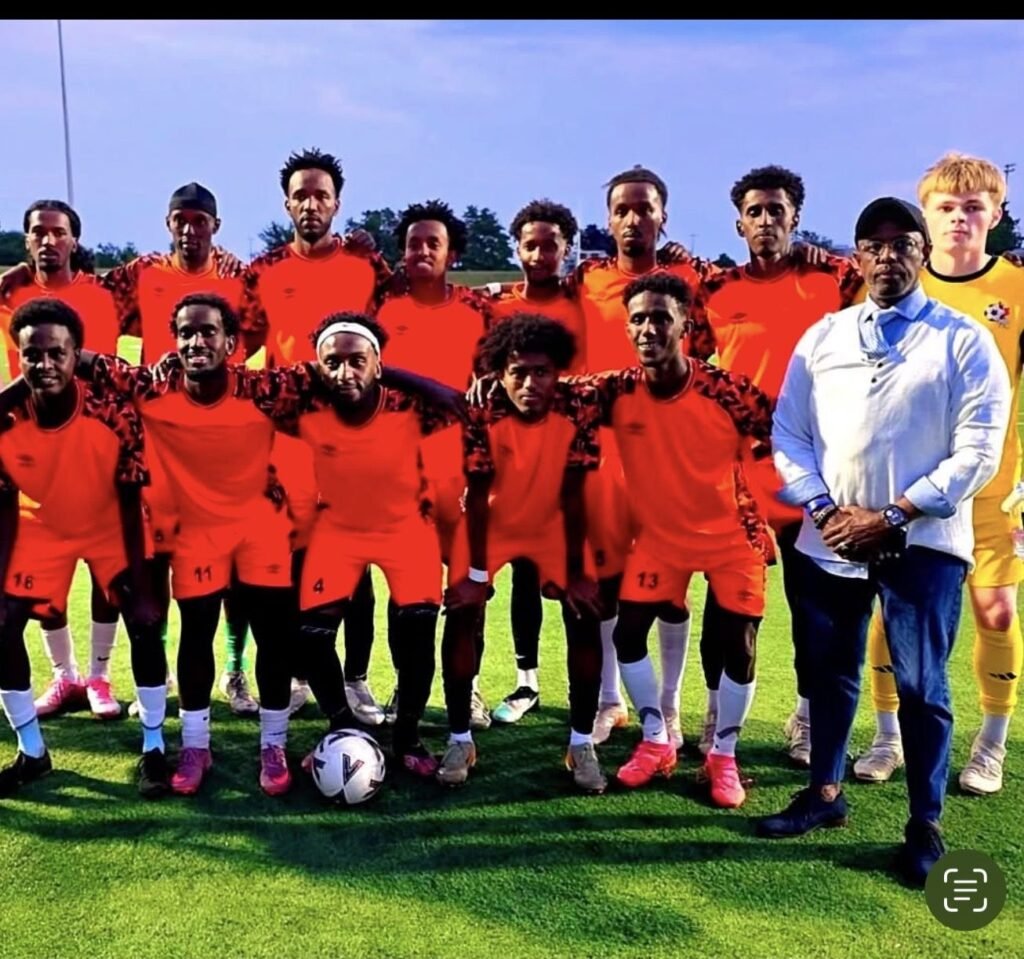 Young men from a community soccer team in orange kits posing on the field with a society leader
