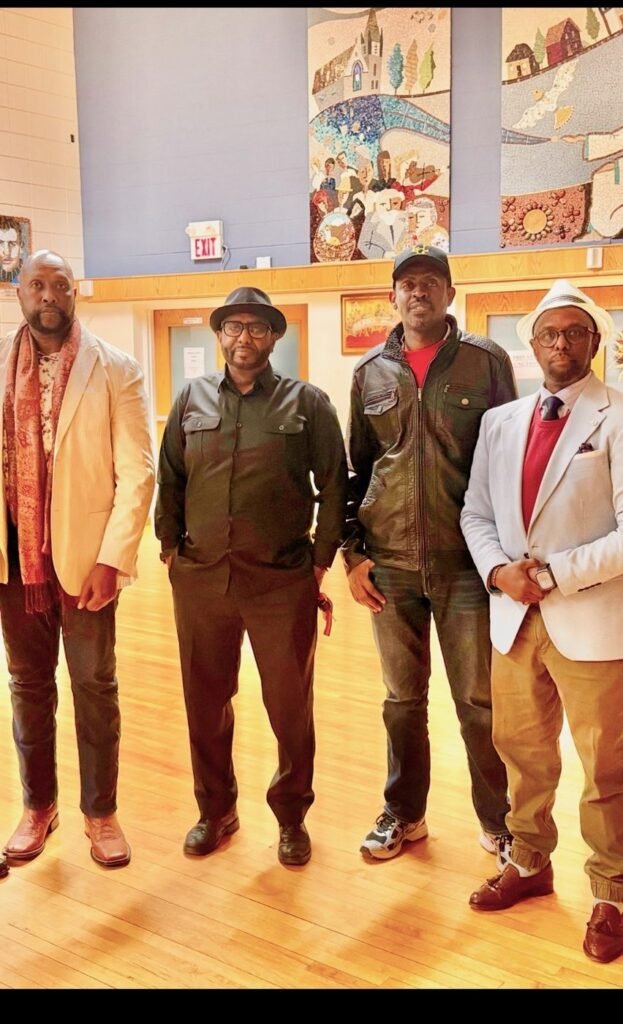 Four community members standing together in a hall with mosaic artwork on the wall