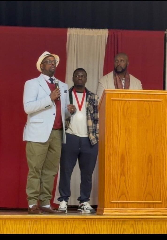 Chairman Ibrahim Shurie speaking into a microphone on stage with two others beside him